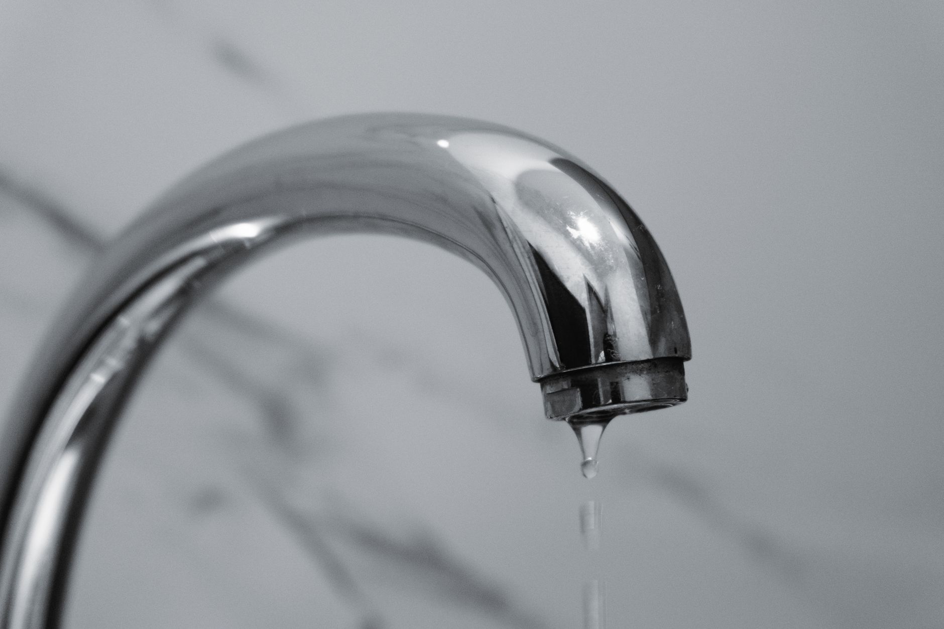 A close-up shot of a modern chrome bathroom faucet with water dripping from the tip.