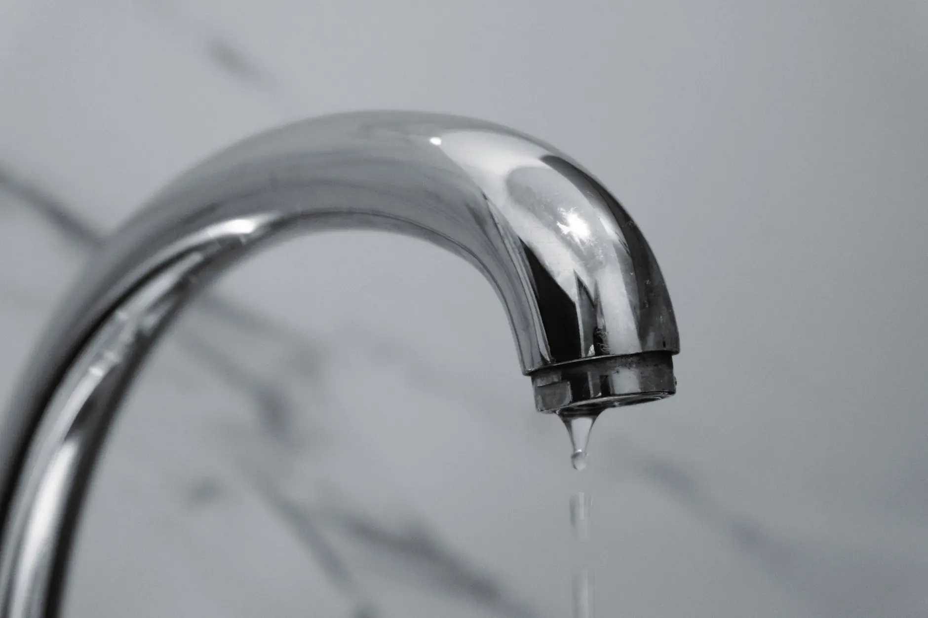A close-up shot of a modern chrome bathroom faucet with water dripping from the tip.