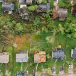 Drone dramatic view of small settlement cottages with ruined roofs and windthrown trees after massive storm
