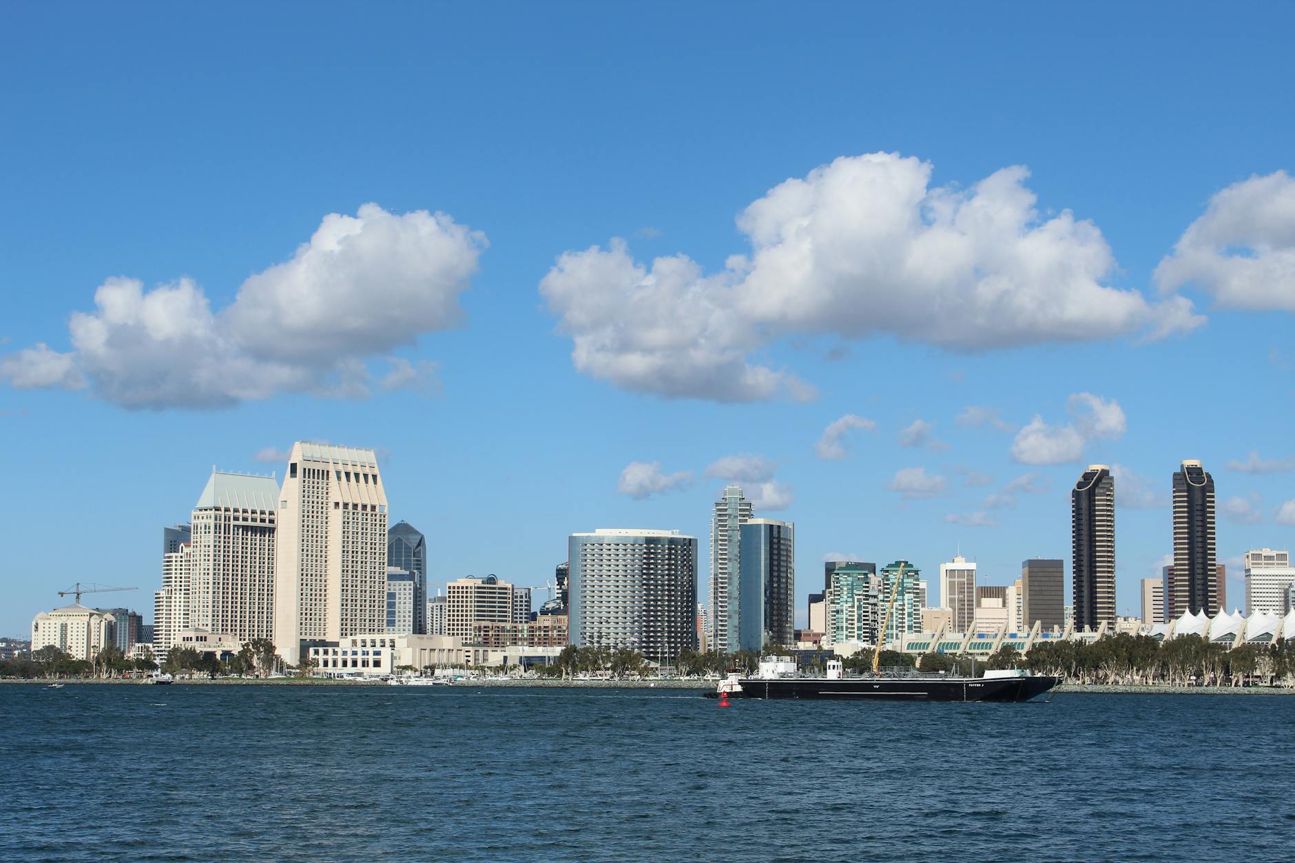 View of San Diego skyline with tall buildings and a ship on a bright day.