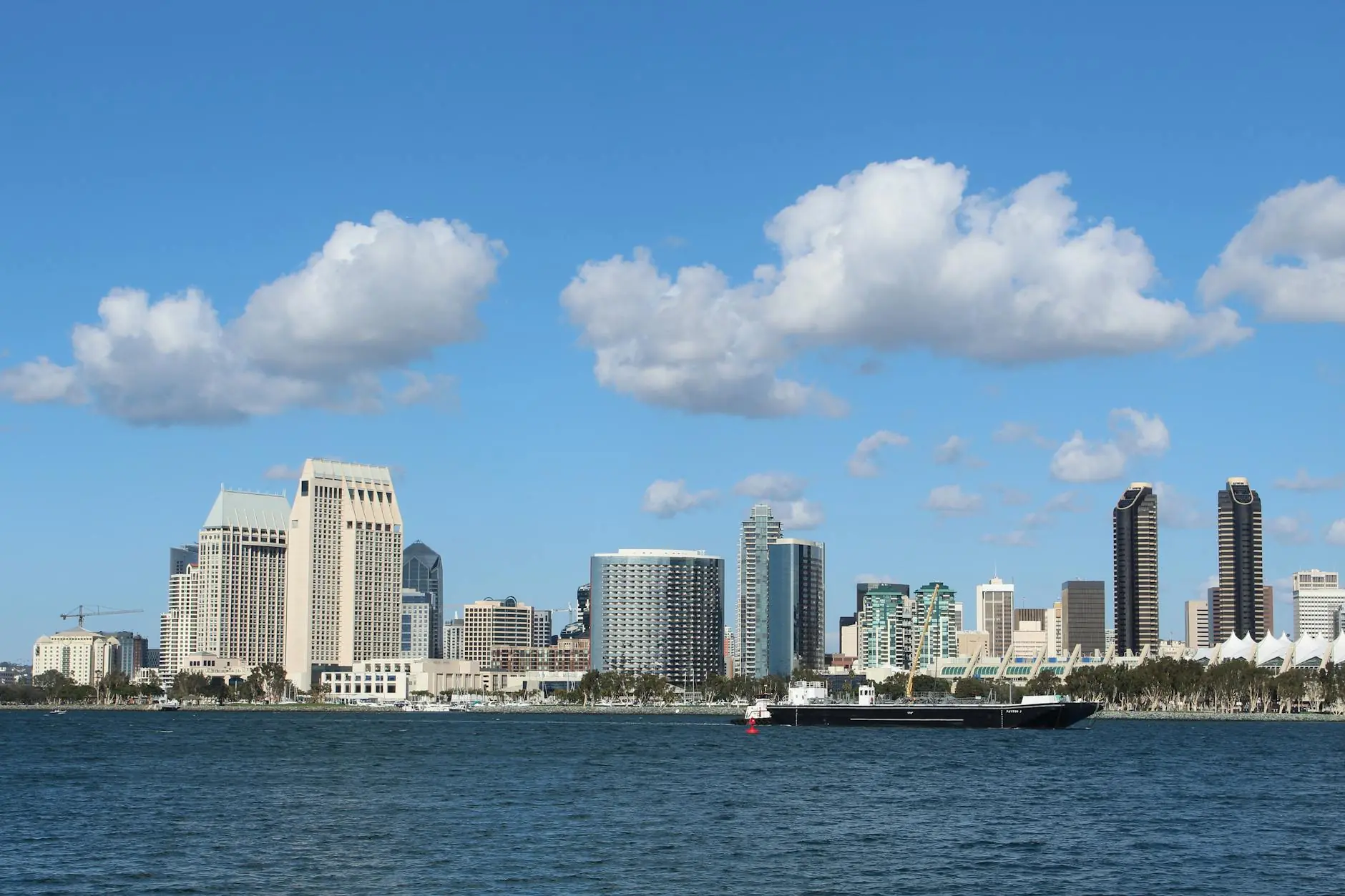 View of San Diego skyline with tall buildings and a ship on a bright day.